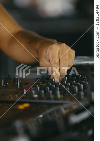 Close up view of a dj's hands playing the mixer while performing in a music festival. 128214494