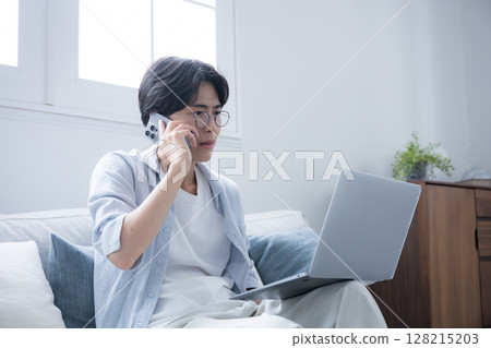A man wearing glasses apologizing while talking on his smartphone and looking at a computer Keyword language: Japanese 128215203