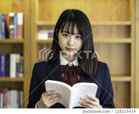 一名高中女生手裡拿著一本書，靜靜地看著鏡頭 | 在圖書館學習的場景 128215414