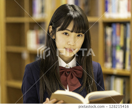 A high school girl smiling gently with a book in her hand | A quiet moment studying in the library 128215416