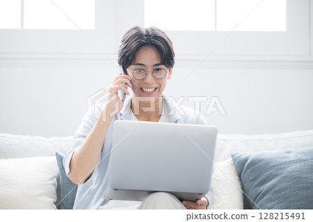 A man smiling and talking on the phone while looking at a computer. Image of a freelancer or busy office worker A man smiling and talking on the phone while looking at a computer. Image of a freelancer or busy office worker 128215491