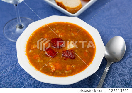 Spicy stewed lentils with suasage and vegetables with thick tomato sauce served in white plate. Spanish cuisine Spicy stewed lentils with suasage and vegetables with thick tomato sauce served in white plate. Spanish cuisine 128215795