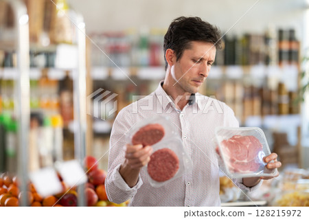 Man in light shirt choose and buy raw cooled beef entrecote and hamburger cutlet in store 128215972