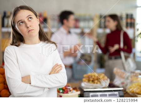 Tired and brassed off girl stands in store and waits for resolution of quarrel between parents. Tired and brassed off girl stands in store and waits for resolution of quarrel between parents. 128215994