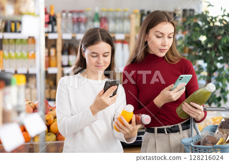 Teenage girl and her mother scanning QR on bottle of smoothie in supermarket Teenage girl and her mother scanning QR on bottle of smoothie in supermarket 128216024