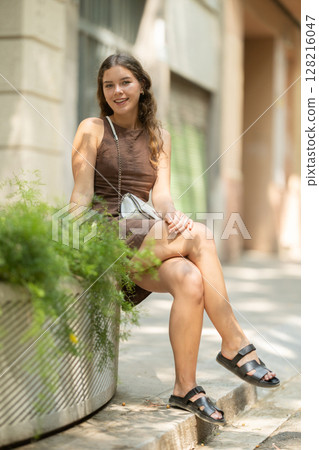 Young woman sitting on a concrete flower bed 128216047