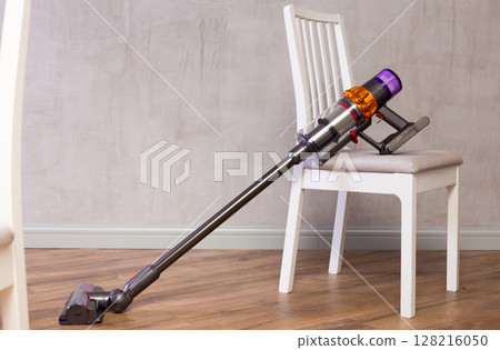 Handheld vacuum cleaner leaned against chair in room Handheld vacuum cleaner leaned against chair in room 128216050