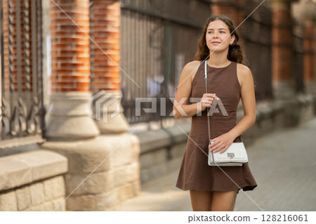 Young woman traveler in summer dress with handbag enjoying walk near columns of architectural complex of Hospital de la Santa Creu i Sant Pau in Barcelona on spring day Young woman traveler in summer dress with handbag enjoying walk near columns of architectural complex of Hospital de la Santa Creu i Sant Pau in Barcelona on spring day 128216061