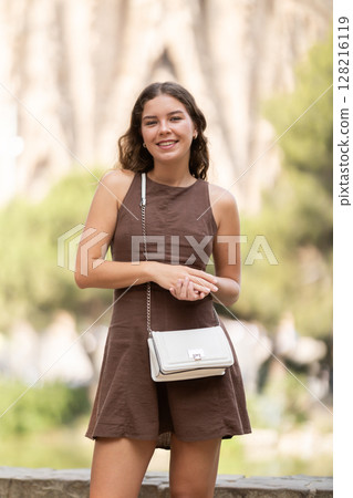 Pretty young woman in summer dress with handbag walking and posing in park on spring day Pretty young woman in summer dress with handbag walking and posing in park on spring day 128216119