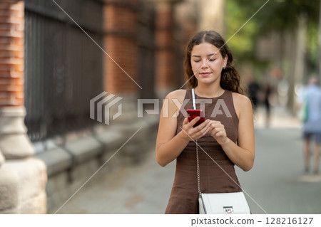 woman walks around the city with a phone in her hands in the summer woman walks around the city with a phone in her hands in the summer 128216127