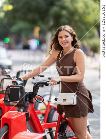 Stylish young girl looking to rent bike while walking through streets of Barcelona 128216153