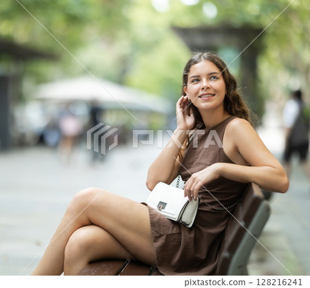 Cheerful young girl resting on bench on street of Barcelona and in summer day 128216241