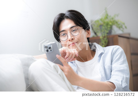 Close-up of handsome man with glasses looking at and holding smartphone 128216572