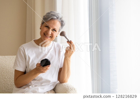 Beautiful smiling elderly woman pensioner during menopause with gray hair applies anti-aging makeup Beautiful smiling elderly woman pensioner during menopause with gray hair applies anti-aging makeup 128216829