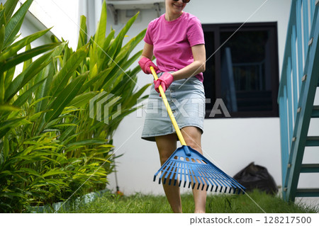 A woman raking the lawn at the backyard of her house A woman raking the lawn at the backyard of her house 128217500