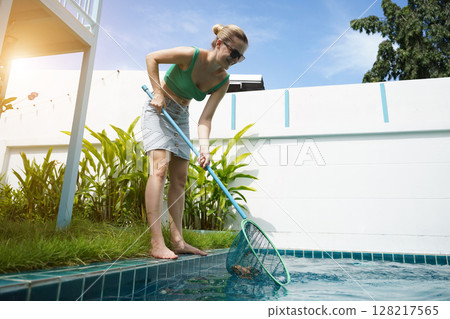 A young woman clean leaves out of a pool  128217565