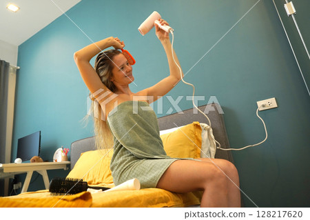 A woman is expertly styling her hair using a blow dryer and brush while in the bathroom A woman is expertly styling her hair using a blow dryer and brush while in the bathroom 128217620