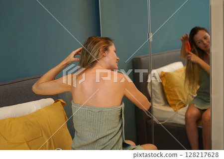 A woman is expertly styling her hair using a blow dryer and brush while in the bathroom A woman is expertly styling her hair using a blow dryer and brush while in the bathroom 128217628