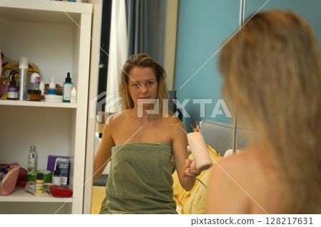 A woman is expertly styling her hair using a blow dryer and brush while in the bathroom A woman is expertly styling her hair using a blow dryer and brush while in the bathroom 128217631