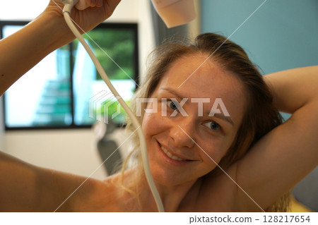 A woman is expertly styling her hair using a blow dryer and brush while in the bathroom 128217654