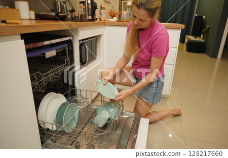 Young woman takes dishes out of the dishwasher machine 128217660