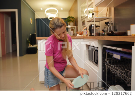 Young woman takes dishes out of the dishwasher machine Young woman takes dishes out of the dishwasher machine 128217662