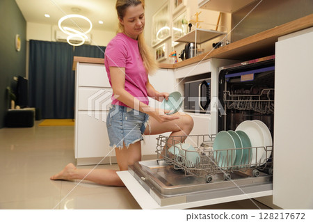 Young woman takes dishes out of the dishwasher machine 128217672