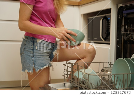Young woman takes dishes out of the dishwasher machine 128217673