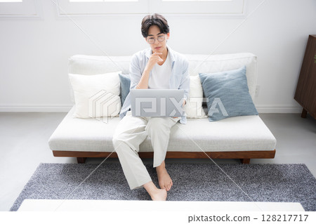 Wide angle of a man's troubled or worried expression as he thinks while looking at a computer Wide angle of a man's troubled or worried expression as he thinks while looking at a computer 128217717