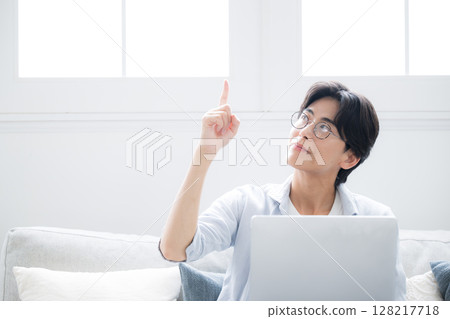Smiling man sitting on sofa in front of a computer, pointing with a bright finger 128217718