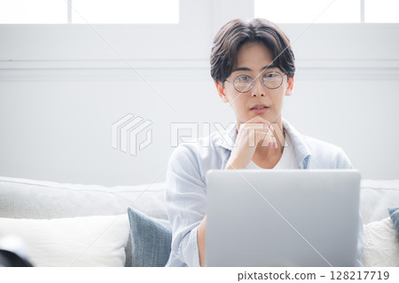 一名男子一邊看著電腦一邊思考。他感到煩惱和憂慮。 128217719