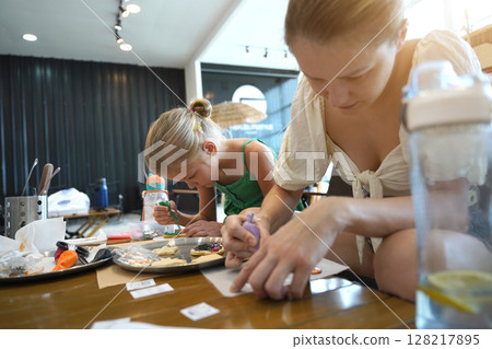 Mother and her daughter paint Halloween cookies  128217895