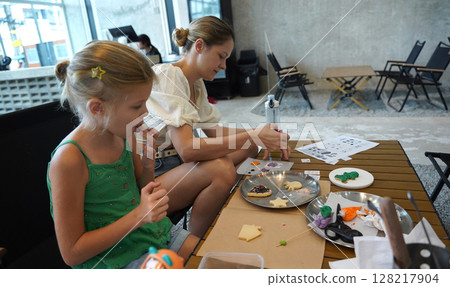 Mother and her daughter paint Halloween cookies  128217904