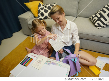 Mother helps her daughter pack her backpack Mother helps her daughter pack her backpack 128218219