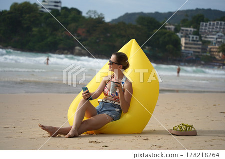 A young woman on the beach lounging on a yellow bean bag A young woman on the beach lounging on a yellow bean bag 128218264