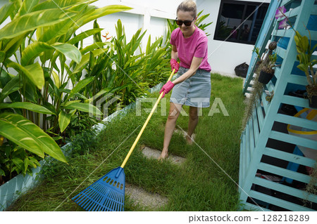 A woman raking the lawn at the backyard of her house A woman raking the lawn at the backyard of her house 128218289