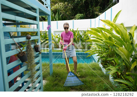 A woman raking the lawn at the backyard of her house  128218292