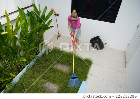 A woman raking the lawn at the backyard of her house A woman raking the lawn at the backyard of her house 128218299