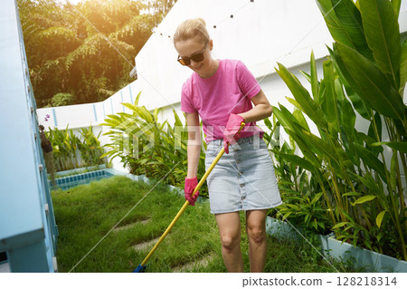 A woman raking the lawn at the backyard of her house  128218314