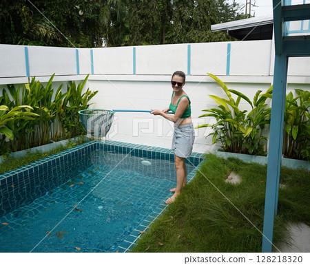 A young woman clean leaves out of a pool  128218320