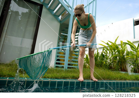 A young woman clean leaves out of a pool A young woman clean leaves out of a pool 128218325
