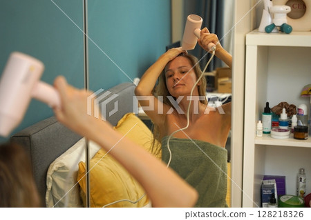 A woman is expertly styling her hair using a blow dryer and brush while in the bathroom A woman is expertly styling her hair using a blow dryer and brush while in the bathroom 128218326
