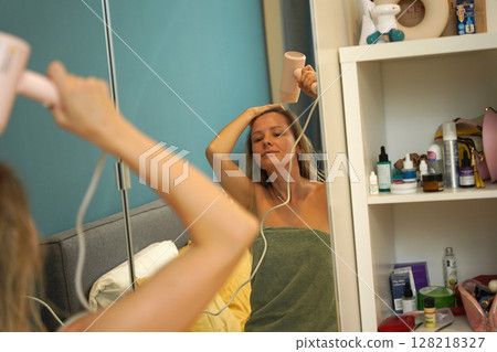 A woman is expertly styling her hair using a blow dryer and brush while in the bathroom 128218327