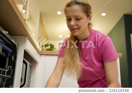 Young woman takes dishes out of the dishwasher machine Young woman takes dishes out of the dishwasher machine 128218398