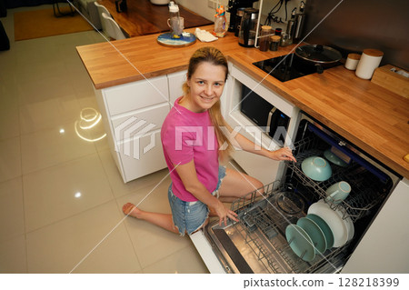 Young woman takes dishes out of the dishwasher machine Young woman takes dishes out of the dishwasher machine 128218399