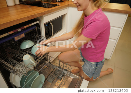 Young woman takes dishes out of the dishwasher machine Young woman takes dishes out of the dishwasher machine 128218403