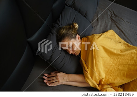 A woman sleeping peacefully under a yellow blanket A woman sleeping peacefully under a yellow blanket 128218499
