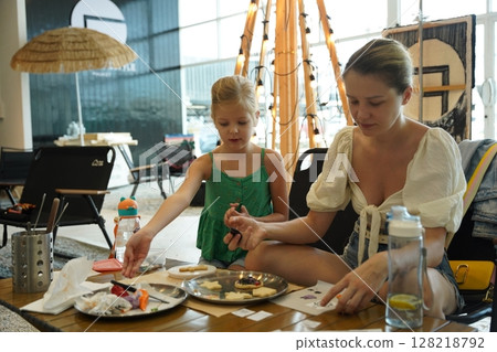 Mother and her daughter paint Halloween cookies  128218792