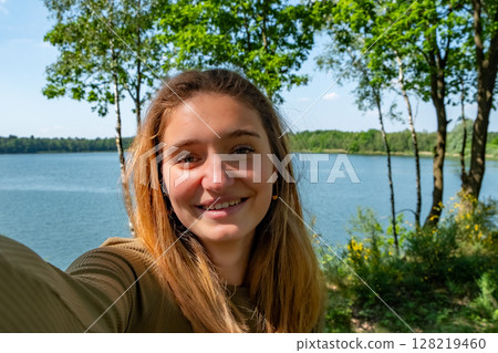 A Smiling Woman Posing Gracefully by the Serene Lake in the Heart of Natures Beauty 128219460