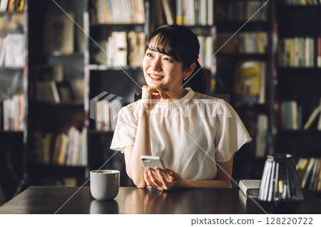 E-books, smartphone in front of bookshelf, young asian woman looking at smartphone E-books, smartphone in front of bookshelf, young asian woman looking at smartphone 128220722